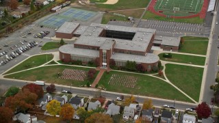 AX117_035E - 5.5K aerial stock footage of orbiting flags at high school in Autumn, Merrick, New York