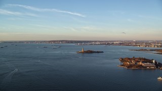 AX118_100E - 5.5K aerial stock footage of Ellis Island and the Statue of Liberty at sunrise in New York