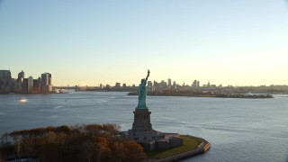 AX118_118 - 5.5K aerial stock footage of flying away from the Statue of Liberty at sunrise in New York