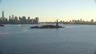 AX118_119E - 5.5K aerial stock footage wide view of Statue of Liberty, and skylines of Brooklyn and Lower Manhattan at sunrise in New York