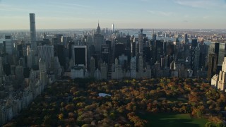 AX118_194E - 5.5K aerial stock footage of Central Park with Autumn leaves and Midtown at sunrise in New York City