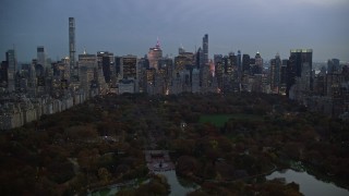 AX121_098E - 5.5K stock footage aerial video of Midtown skyscrapers seen from The Lake in Central Park at twilight, New York City