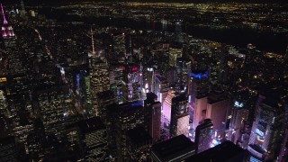 AX122_115E - 5.5K aerial stock footage of circling the Bank of America Tower toward the glow of Times Square at Night, Midtown, NYC