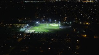 AX123_157E - 5.5K aerial stock footage of flying over suburban homes toward baseball fields at Night in Hempstead, New York