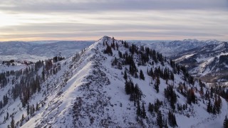 AX124_121E - 5.5K aerial stock footage fly over Clayton Peak with winter snow and reveal valley at sunrise in the Wasatch Range, Utah