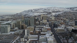 AX124_213 - 5.5K stock footage aerial video approach buildings in Downtown Salt Lake City with snow at sunrise in Utah