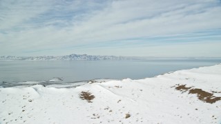 AX125_038E - 5.5K aerial stock footage of the Great Salt Lake seen from snowy mountain summit on Antelope Island, Utah