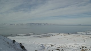 AX125_040 - 5.5K aerial stock footage of Great Salt Lake seen from snowy ridge on Antelope Island in winter, Utah