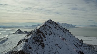 AX125_048E - 5.5K aerial stock footage fly over snowy Antelope Island ridge and peak toward Great Salt Lake in winter, Utah