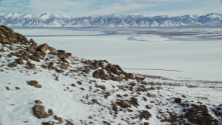 AX125_069 - 5.5K aerial stock footage track a bighorn sheep racing down a rocky slope with winter snow, Antelope Island, Utah