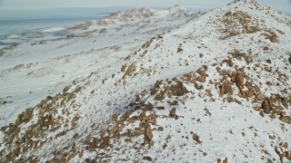 AX125_073 - 5.5K aerial stock footage of orbiting a snowy, rocky mountain slope on Antelope Island, Utah