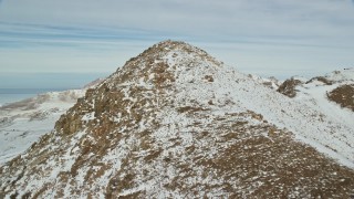 AX125_079E - 5.5K aerial stock footage approach and fly over stony mountain peak with winter snow, Antelope Island, Utah