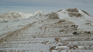 AX125_086 - 5.5K aerial stock footage fly over rocky ground and snow to approach mountains in winter, Antelope Island, Utah