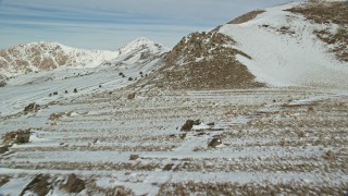 AX125_086E - 5.5K aerial stock footage fly over rocky ground and snow up the slopes of mountains in winter, Antelope Island, Utah