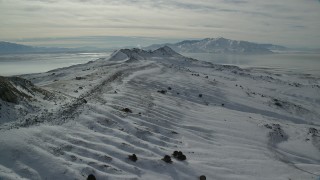 AX125_090 - 5.5K aerial stock footage fly over snowy ground toward wintery mountains, Antelope Island, Utah