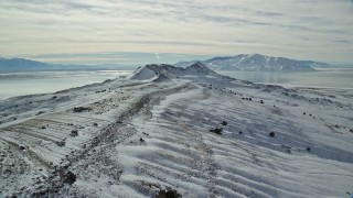 AX125_090E - 5.5K aerial stock footage fly over snowy ground toward wintery mountains, Antelope Island, Utah
