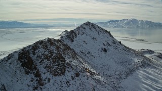 AX125_096E - 5.5K aerial stock footage approach and fly over snowy peak near shore of Great Salt Lake, Antelope Island, Utah