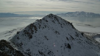 AX125_097 - 5.5K aerial stock footage approach and fly over snowy peak near shore of Great Salt Lake, Antelope Island, Utah