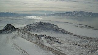 AX125_098 - 5.5K aerial stock footage of a small snowy mountain near Great Salt Lake shore in winter, Antelope Island, Utah