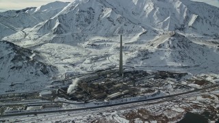 AX125_110E - 5.5K aerial stock footage of approaching tall factory smoke stack and Oquirrh Mountains in wintertime, Magna, Utah