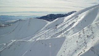 AX125_126 - 5.5K aerial stock footage of sunlight on snowy Kessler Peak slopes in winter, Utah