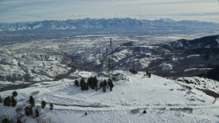 AX125_137E - 5.5K aerial stock footage orbit radio towers on snowy peak with light snowdrifts in winter, Oquirrh Mountains, Utah