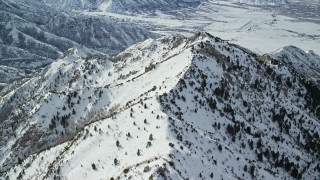 AX125_148E - 5.5K aerial stock footage of following a snowy mountain ridge dotted with evergreens in winter, Oquirrh Mountains, Utah