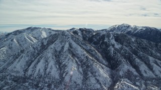 AX125_169E - 5.5K aerial stock footage of slowly passing by Oquirrh Mountains with winter snow in Utah