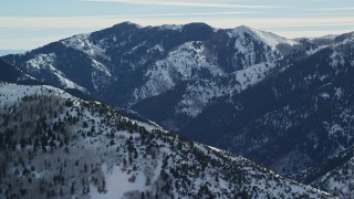 AX125_174E - 5.5K aerial stock footage of snowy peak seen by an Oquirrh Mountains ridge, Utah