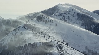 AX125_180E - 5.5K aerial stock footage of snowdrift plumes rising from Oquirrh Mountains peaks in winter, Utah