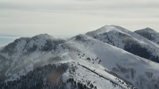 AX125_184 - 5.5K aerial stock footage of Oquirrh Mountains peaks with winter snowdrifts in Utah
