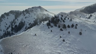 AX125_190E - 5.5K aerial stock footage of snowdrifts blowing from slope in the Oquirrh Mountains, Utah
