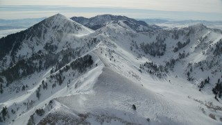 AX125_203 - 5.5K aerial stock footage of flying over a mountain ridge with snowdrifts, approach Lowe Peak in winter, Utah