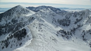 AX125_203E - 5.5K aerial stock footage of flying over a mountain ridge with snowdrifts, approach Lowe Peak in winter, Utah