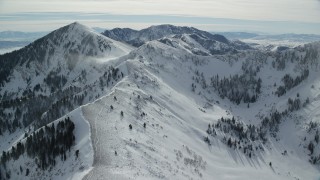 AX125_204 - 5.5K aerial stock footage fly over snowy mountain ridge and pan to snowdrifts and Lowe Peak, Utah