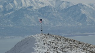 AX125_211 - 5.5K aerial stock footage orbit American flag on summit of snowy Oquirrh Mountains peak, Utah