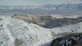 AX125_226 - 5.5K aerial stock footage orbit Bingham Canyon Mine beyond snowy mountain ridge in winter, Utah