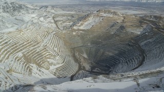 AX125_230 - 5.5K stock footage aerial video orbit rim of Bingham Canyon Mine in Utah with light winter snow
