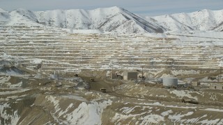 AX125_246 - 5.5K aerial stock footage orbit Bingham Canyon Mine with gravel haulers on a dirt road in winter, Utah