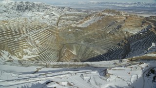 AX125_260E - 5.5K aerial stock footage fly over snowy mountain ridge to reveal enormous open pit copper mine with winter snow, Utah