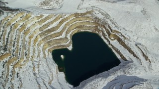 AX125_274E - 5.5K aerial stock footage approach open pit mIne filled with water and tilt down in winter, Oquirrh Mountains, Utah