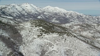 AX125_278E - 5.5K aerial stock footage of snowy Farnsworth and Kessler Peaks seen from smaller peaks in winter, Utah