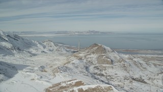 AX125_292 - 5.5K aerial stock footage fly over snowy mountains to approach Kennecott Smokestack in winter, Magna, Utah