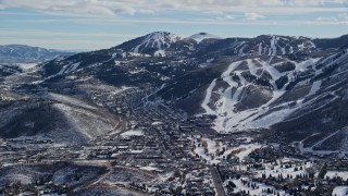 AX126_159E - 5.5K aerial stock footage a small town between snowy hills and mountains in winter, Park City, Utah