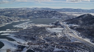 AX126_177E - 5.5K aerial stock footage approach condos and highway near the shore of Jordanelle reservoir with winter snow, Heber City, Utah