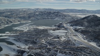 AX126_178 - 5.5K aerial stock footage approach condos and highway near the shore of Jordanelle reservoir with winter snow, Heber City, Utah