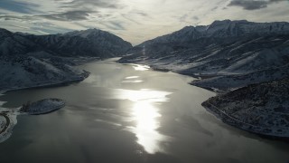 AX126_224 - 5.5K aerial stock footage of sun reflecting off of icy Deer Creek Reservoir in wintertime, Utah