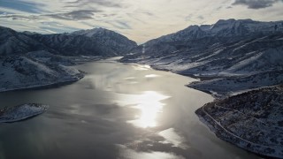 AX126_224E - 5.5K aerial stock footage of sun reflecting off of icy Deer Creek Reservoir in wintertime, Utah