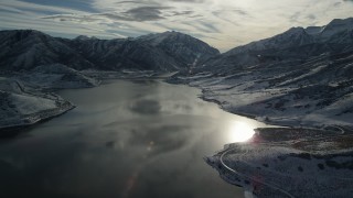 AX126_226 - 5.5K aerial stock footage video of sunlight and ice on a reservoir with snow mountains on the shore in winter, Utah