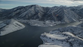 AX126_231 - 5.5K aerial stock footage orbit frozen shores of a reservoir near snowy mountains in wintertime, Utah